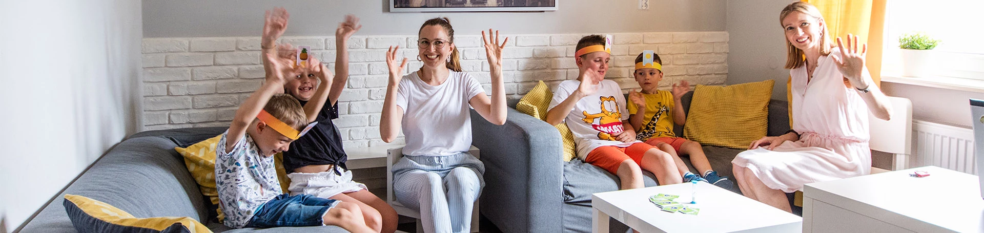 Dwie kobiety i czwórka chłopców siedzący na sofach. Uśmiechnięci, machają w kierunku obiektywu.