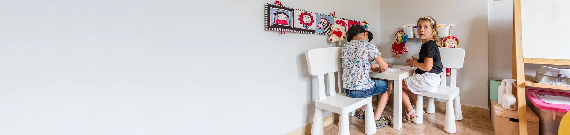 Chłopiec i dziewczynka rysujący przy małym białym stoliku.